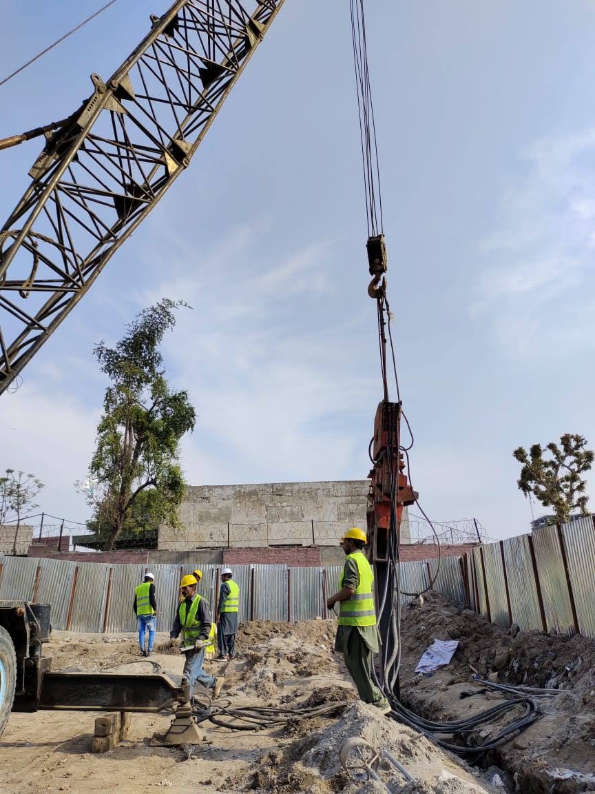 Piling rig with crawler crane and site crew in high-visibility vests at the JICA-funded Faisalabad project