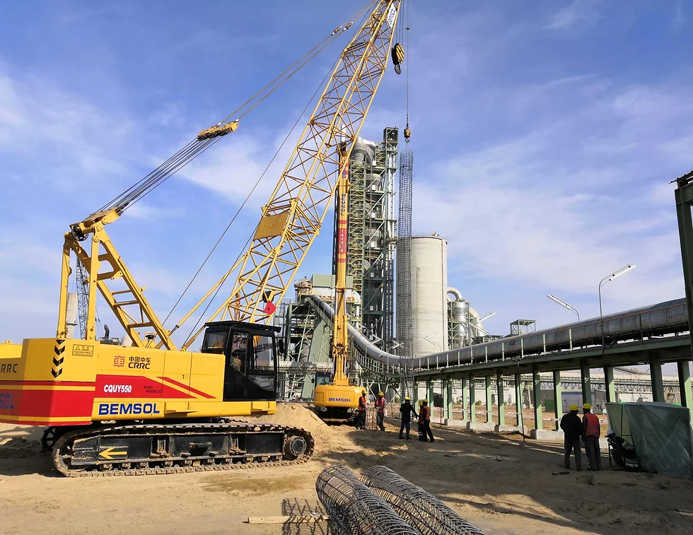 Crawler crane lifting reinforcement cages beside cement plant silos